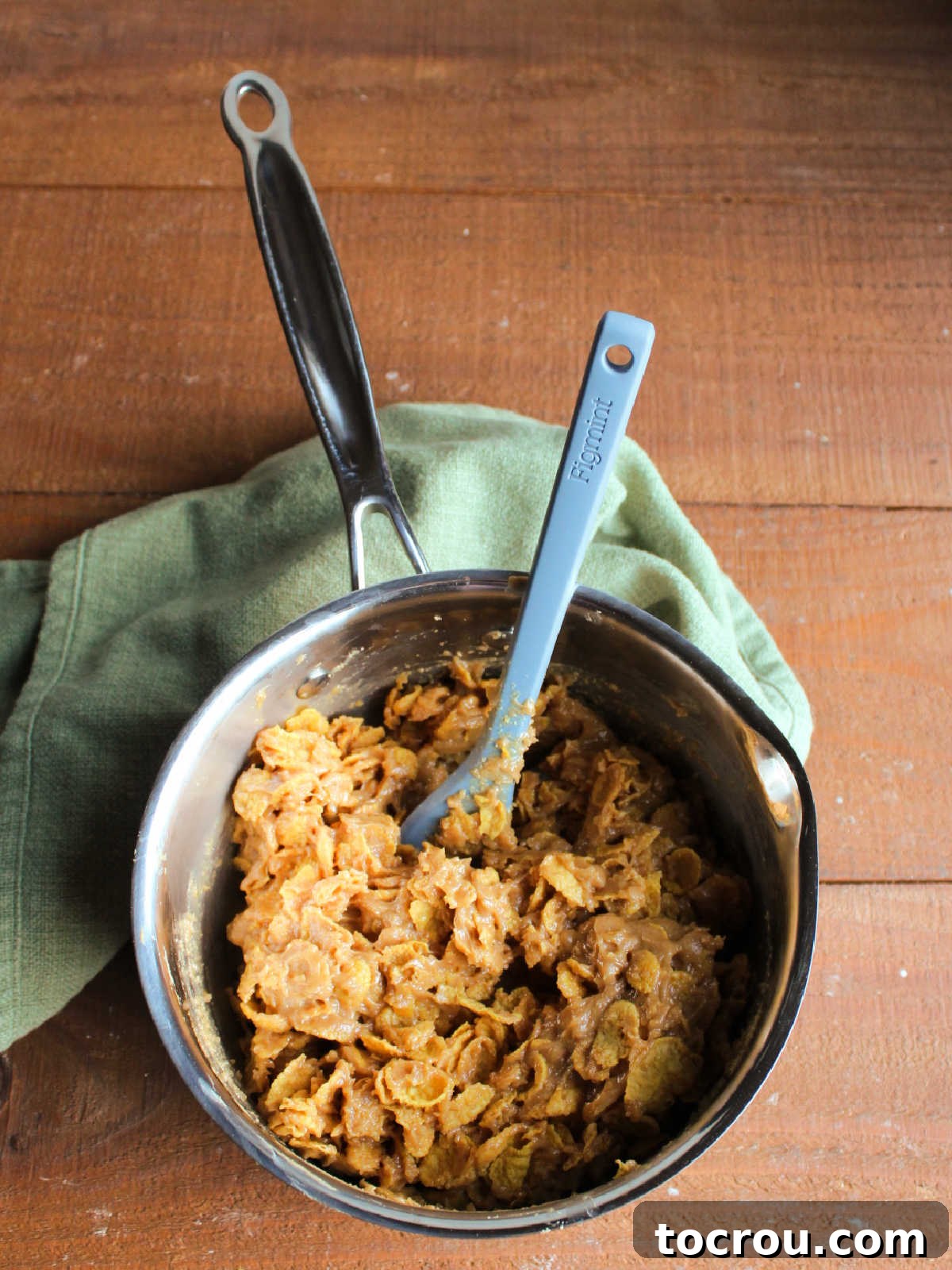 Mixing crispy cornflakes into the sweet peanut butter. Peanut butter and cornflake mixture in a saucepan, ready to be pressed into the baking pan.