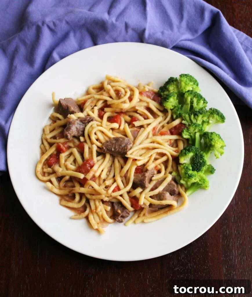 A hearty plate of egg noodles cooked in a savory beef and tomato sauce, garnished with fresh broccoli florets.