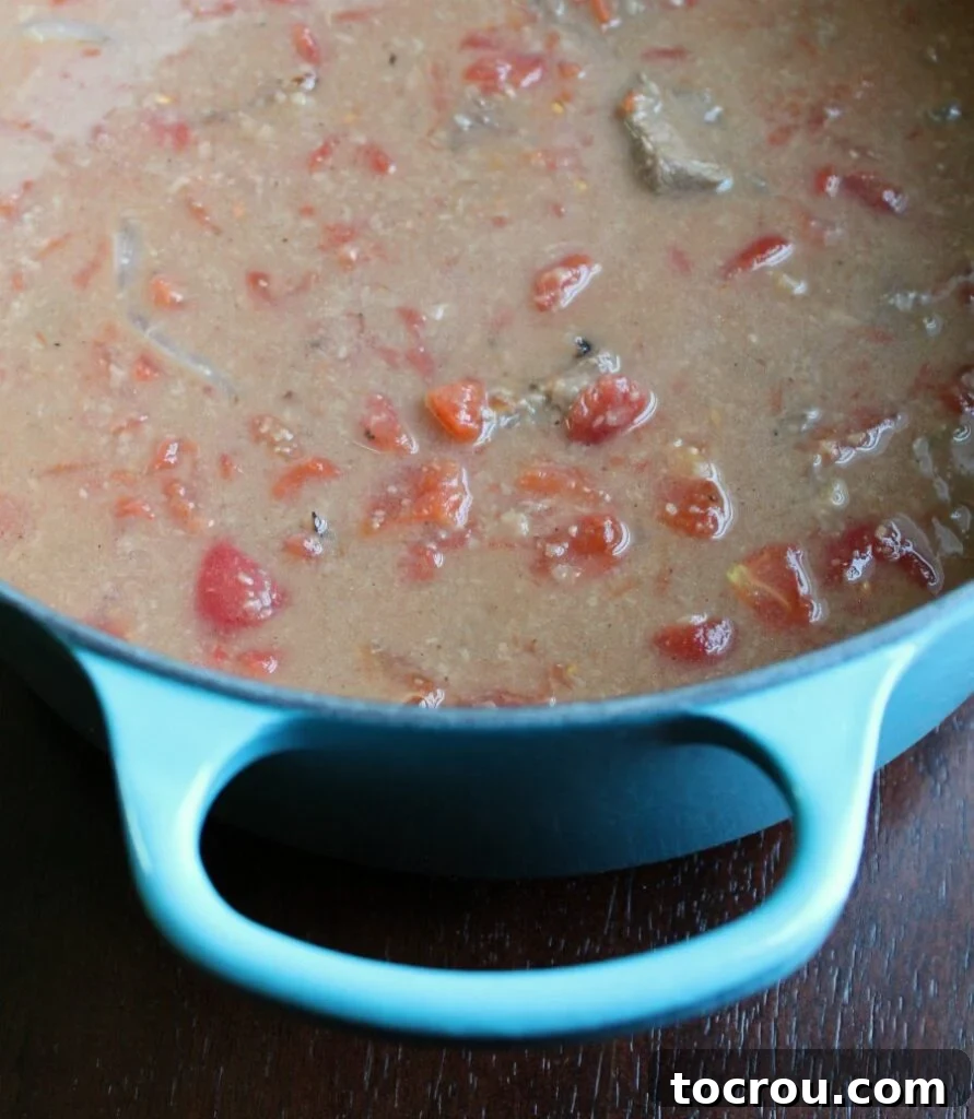 A rich, saucy mixture of tender beef and stewed tomatoes simmering perfectly in a Dutch oven.