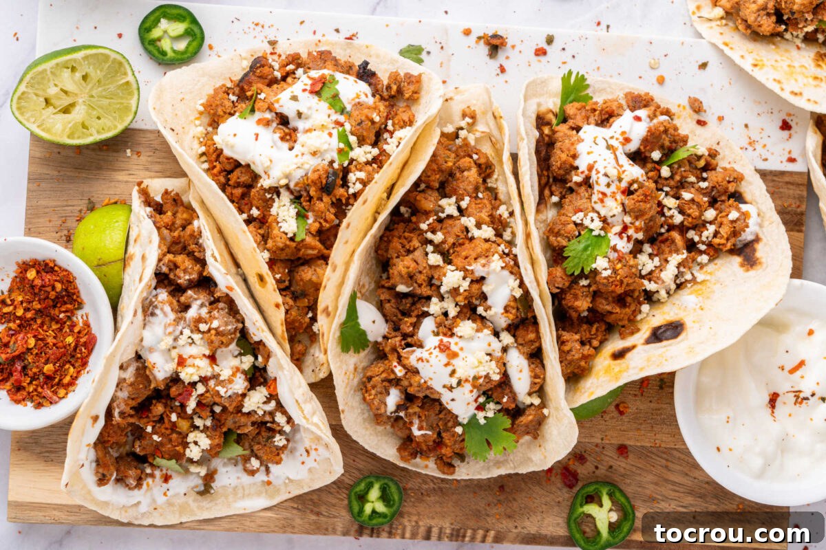 Wooden cutting board with four chorizo tacos, a lime half, sliced jalapeno, and red pepper flakes nearby for adding to the tacos. The tacos are generously filled with reddish-brown chorizo and garnished with fresh cilantro, inviting a delicious meal.