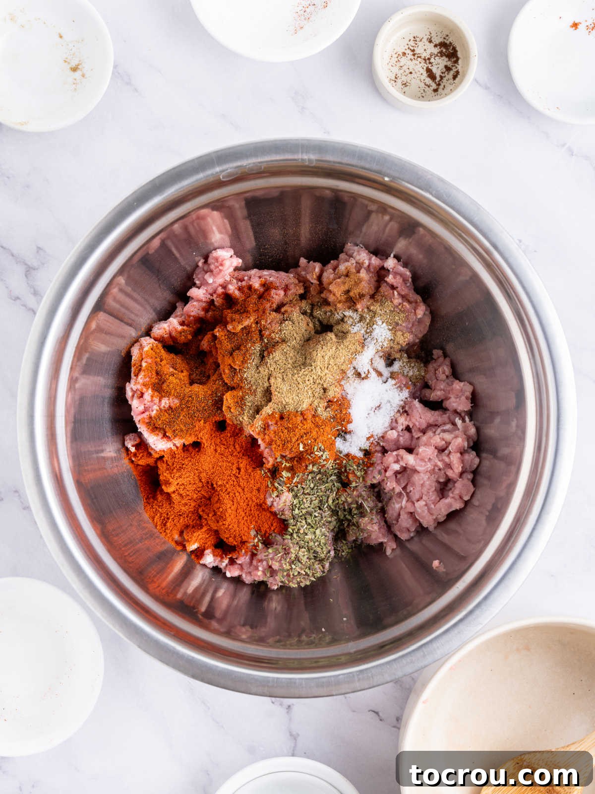 A bowl of ground pork mixed thoroughly with a blend of vibrant red and brown seasonings, transforming it into fresh chorizo sausage, demonstrating the first step in creating homemade chorizo.