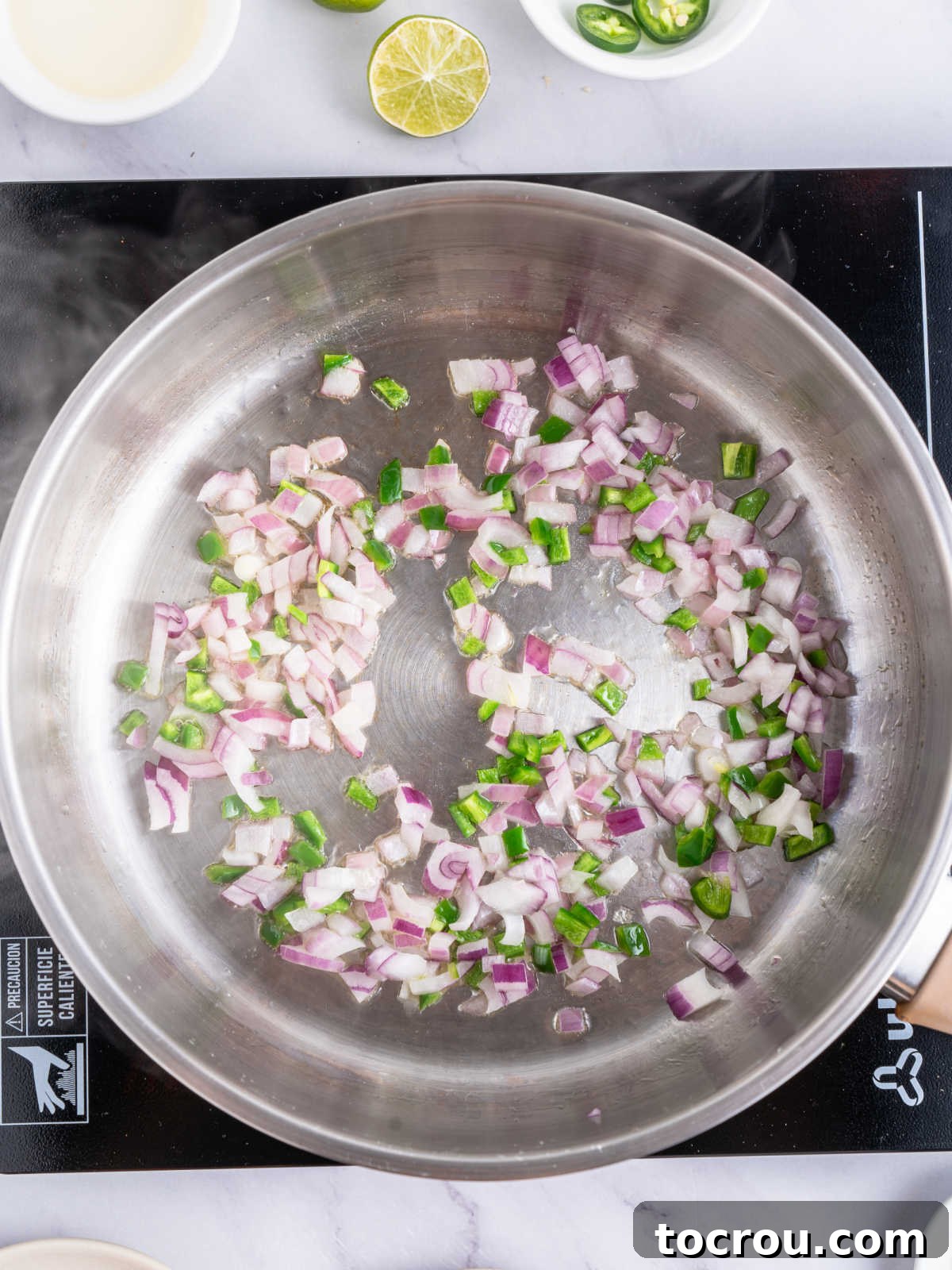 A cast iron skillet on a stovetop, filled with finely diced red onion and green jalapeno peppers, sizzling gently as they cook down to a softened, translucent state, releasing their aromas.