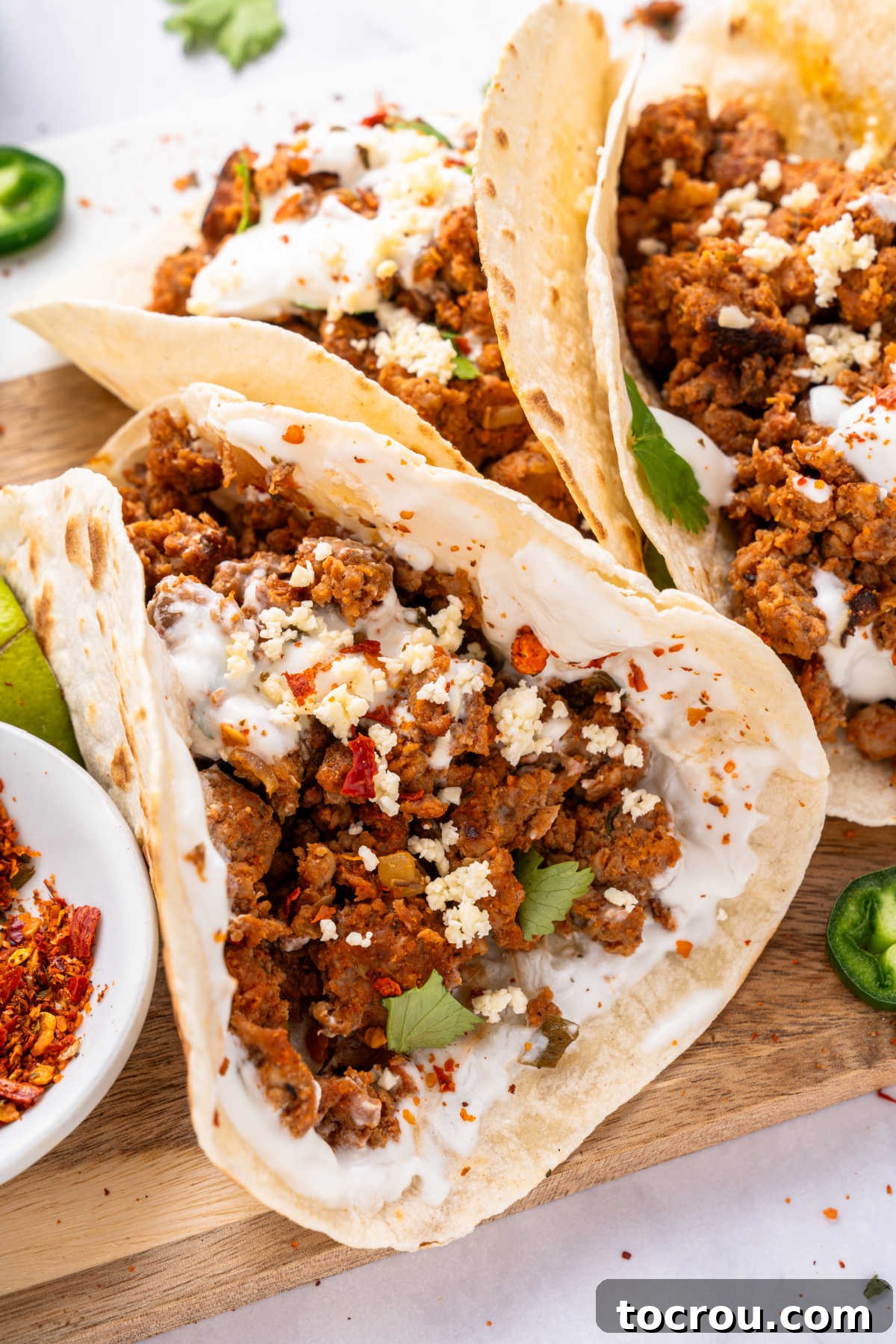 A close-up shot of a perfectly assembled chorizo taco, featuring a warm tortilla spread with sour cream, generously filled with crumbled chorizo, topped with fresh cotija cheese and a sprinkle of vibrant cilantro, ready to be enjoyed.