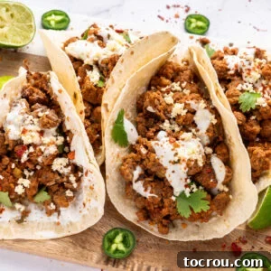 Close up of chorizo tacos with sour cream spread over tortilla, reddish chorizo, crumbled white queso fresco, cilantro, and jalapeno slices, showcasing a beautifully garnished and inviting taco.