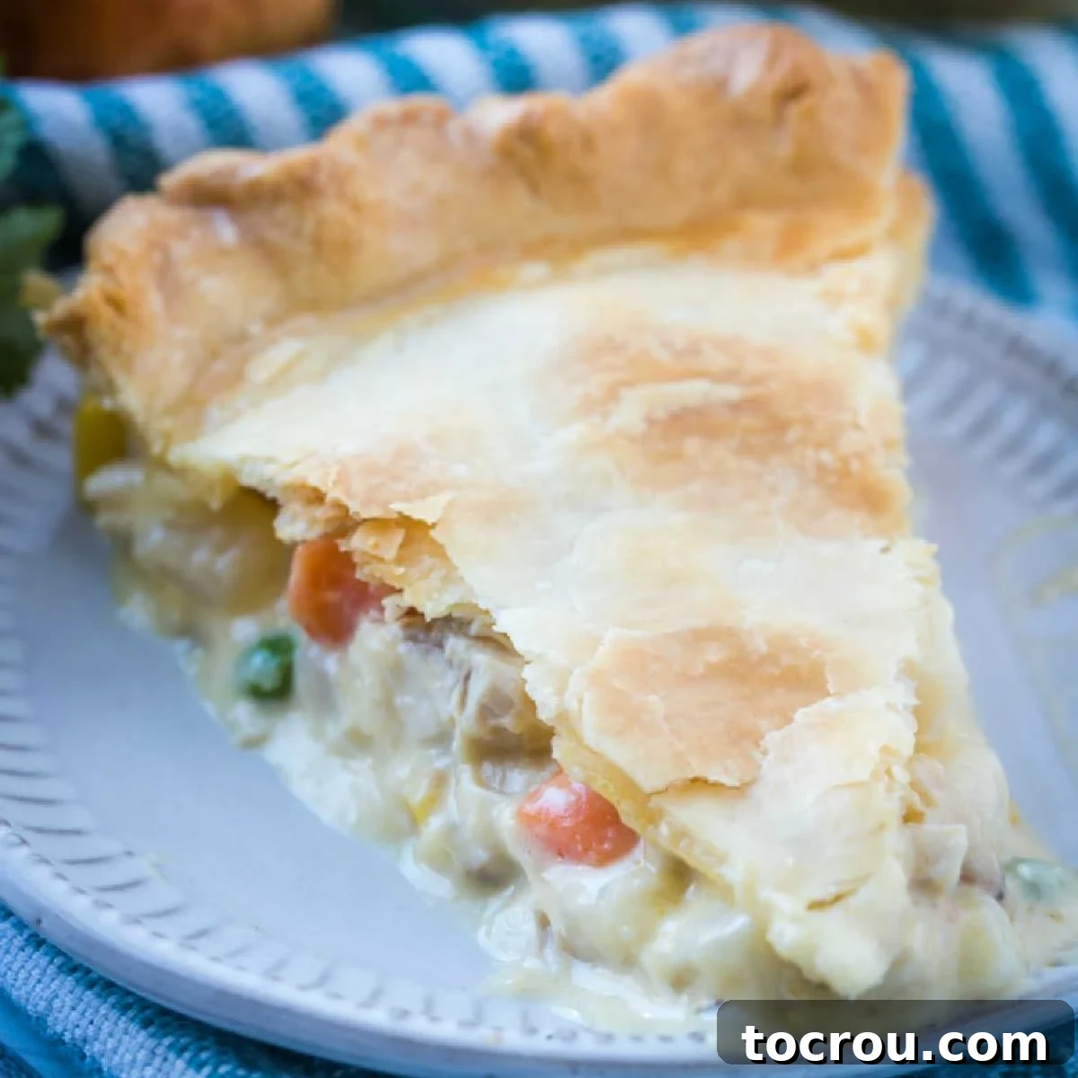 A golden-brown slice of creamy chicken pot pie, revealing a rich filling of chicken and mixed vegetables.
