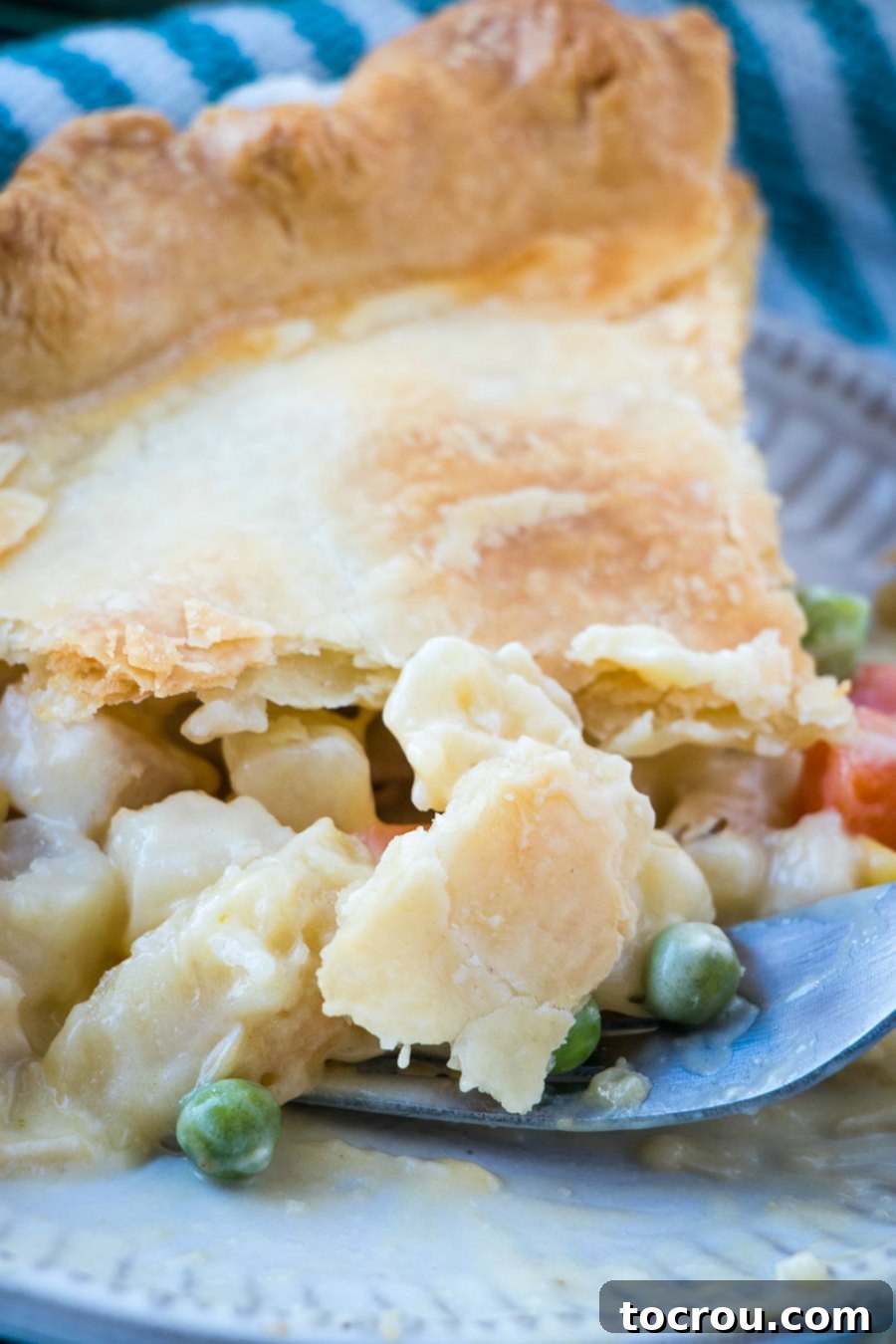 A fork lifts a generous bite of creamy chicken pot pie, showcasing tender chicken, vegetables, and potatoes within the rich filling.