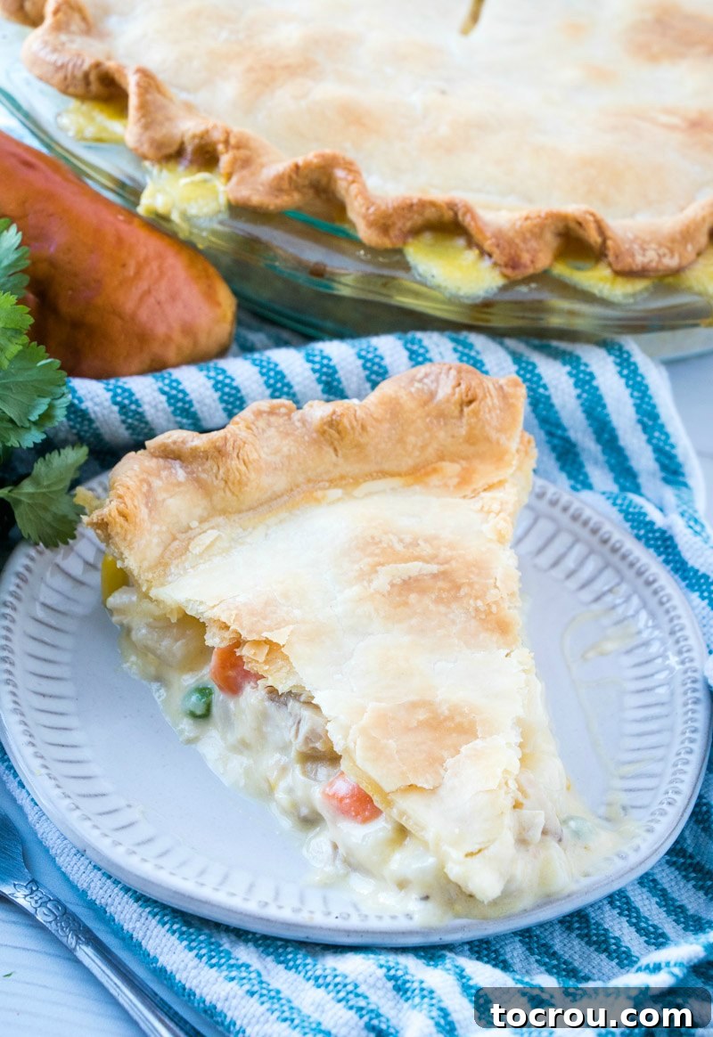 A close-up of a generous piece of chicken pot pie, showing the abundant creamy filling with visible chunks of chicken, vegetables, and potatoes, ready to be enjoyed.