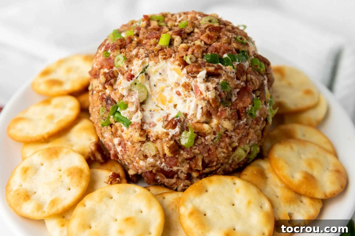 Cheddar bacon ranch cheese ball coated in green onions and pecans with a little bit missing showing the cheesy inside.