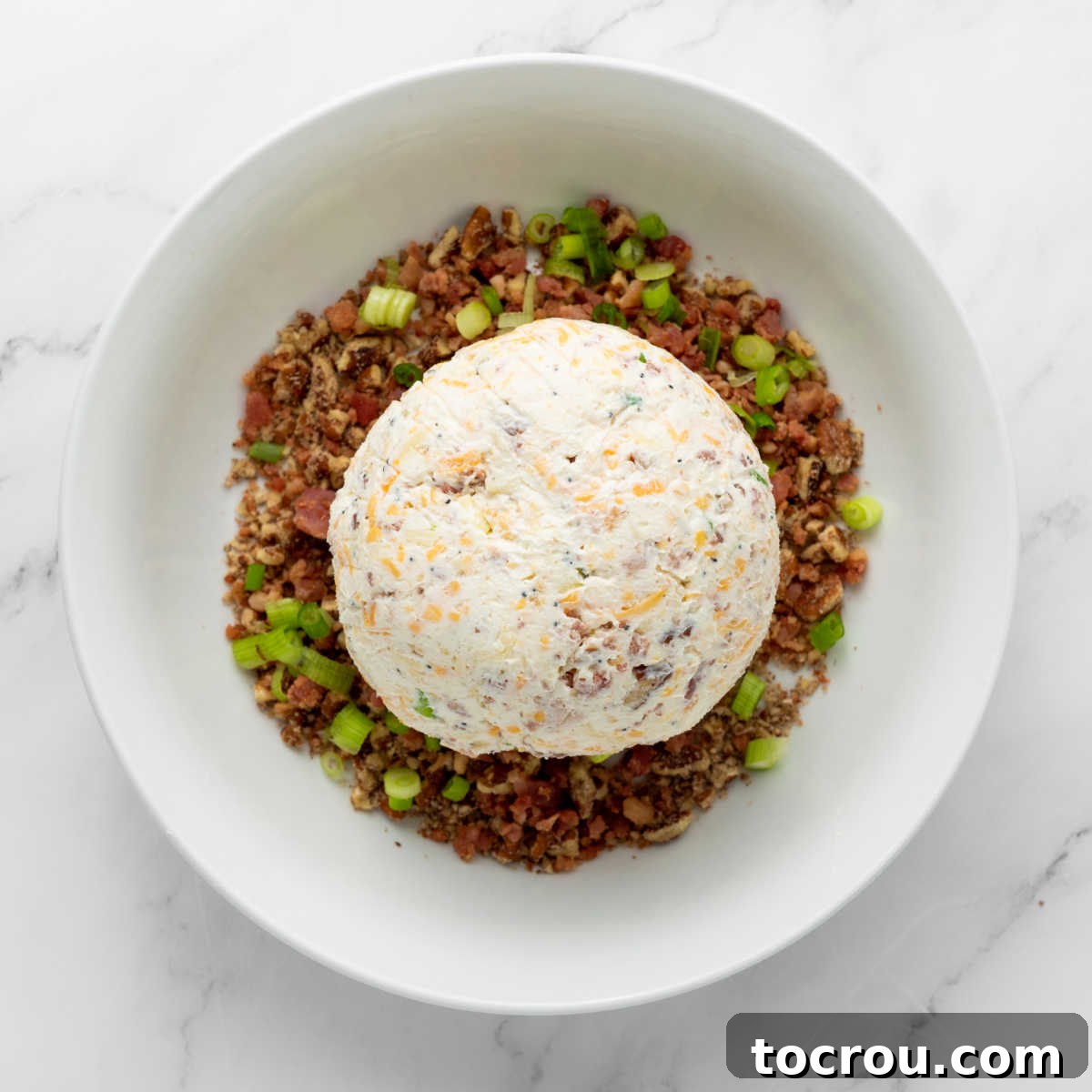 Chilled cheese ball in bowl with chopped pecans and green onions.