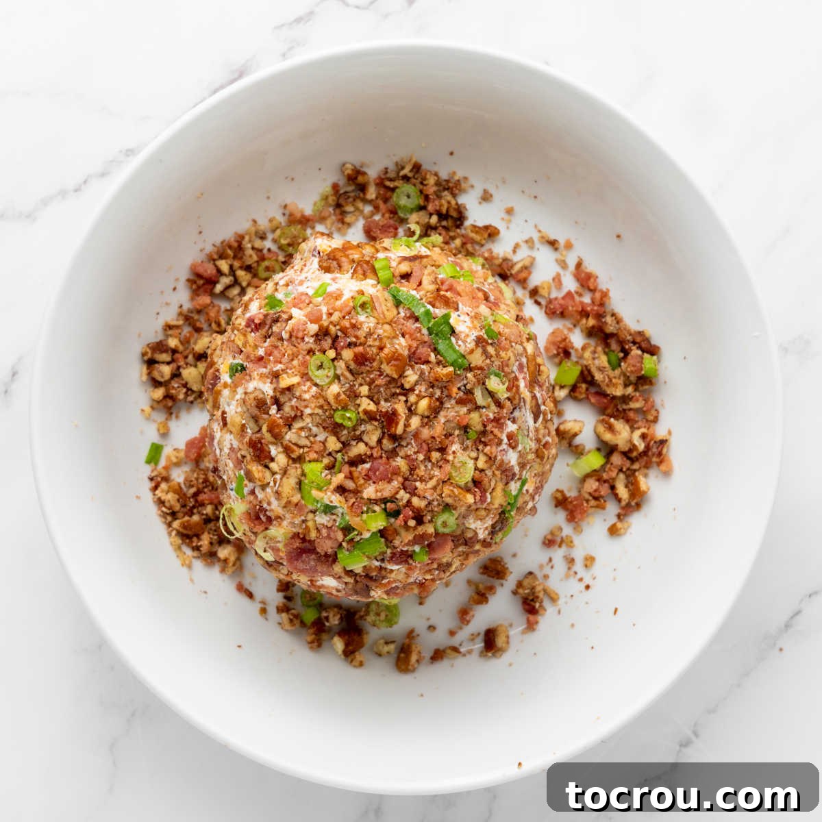 Cheese ball being rolled in coating of pecans and green onions.