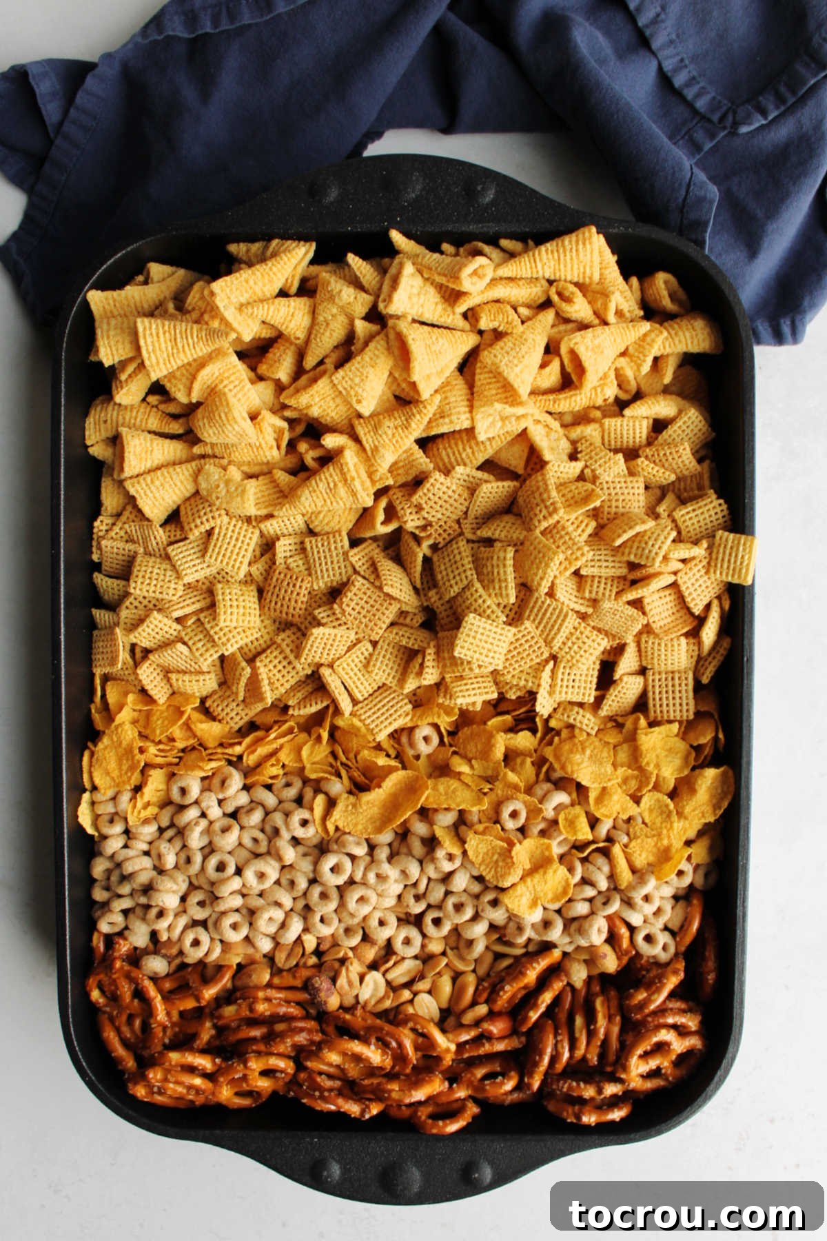 Pan filled with bugles, pretzels, Chex, peanuts, cornflakes and Cheerios ready to be coated in caramel mixture for caramel chex mix.
