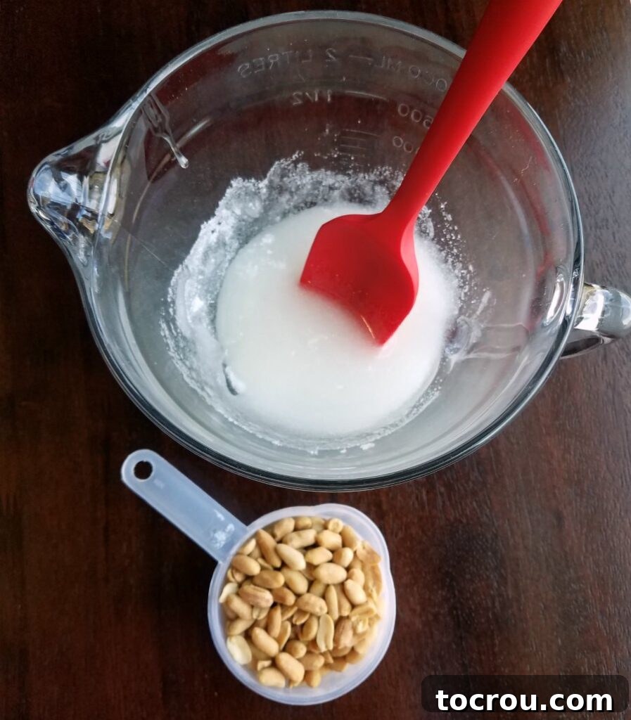 Sugar and corn syrup mixture in a glass bowl next to a measuring cup of peanuts, ready for microwaving.