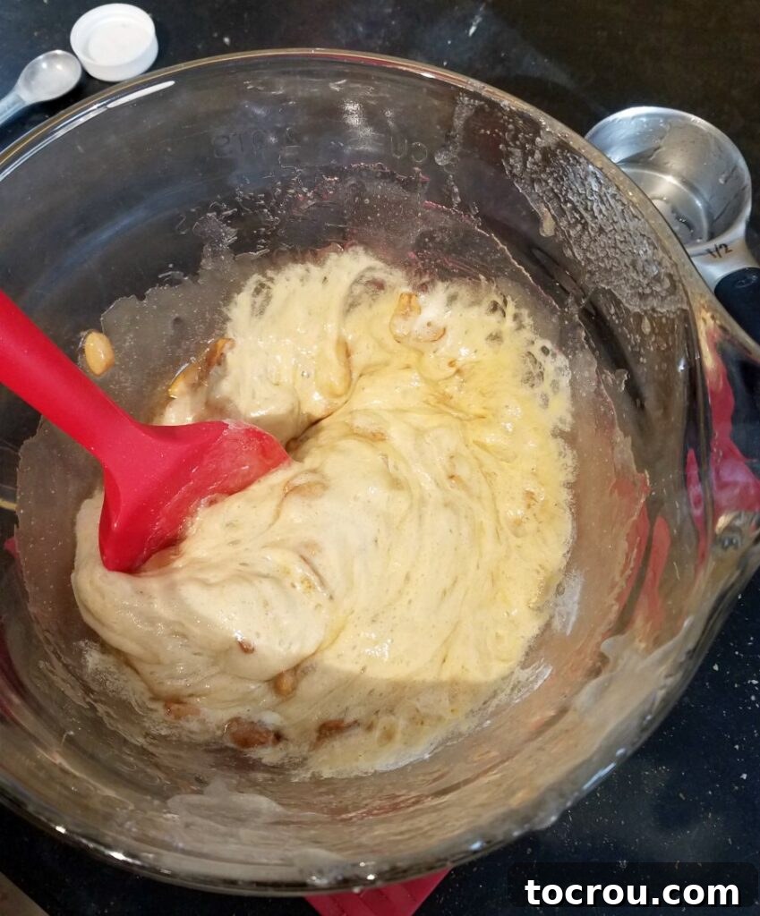 Foamy, hot peanut brittle mixture in a glass bowl after stirring in baking soda, showing the aeration process.