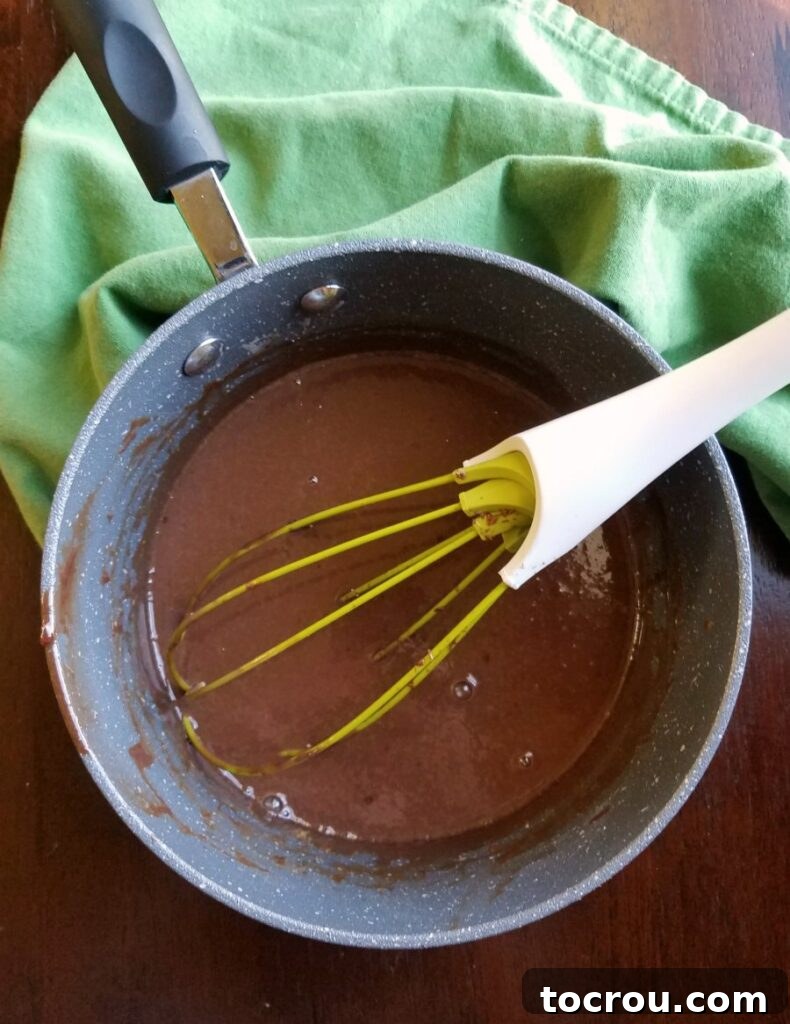 Melted Frango Mint Custard in Saucepan Smooth, melted Frango mint chocolate custard gently stirred in a gleaming stainless steel saucepan with a whisk, showing its rich, glossy texture.