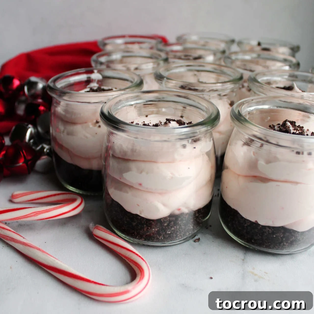 Jars of peppermint no bake cheesecake with chocolate crust and candy cane filling ready to eat, garnished with extra crushed candy canes and fresh mint.