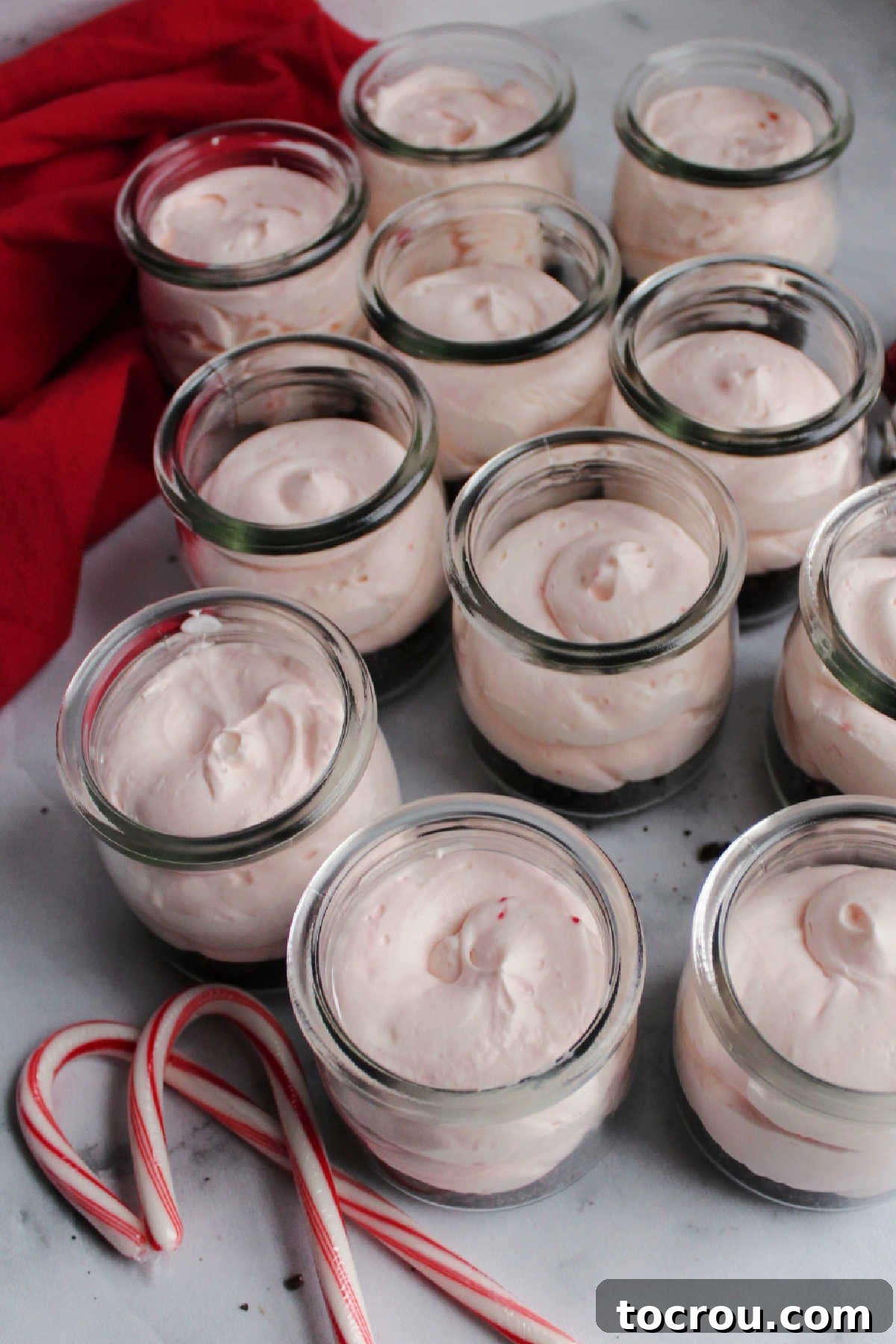 Jars of no bake candy cane cheesecake being assembled, ready to go in the refrigerator to chill.
