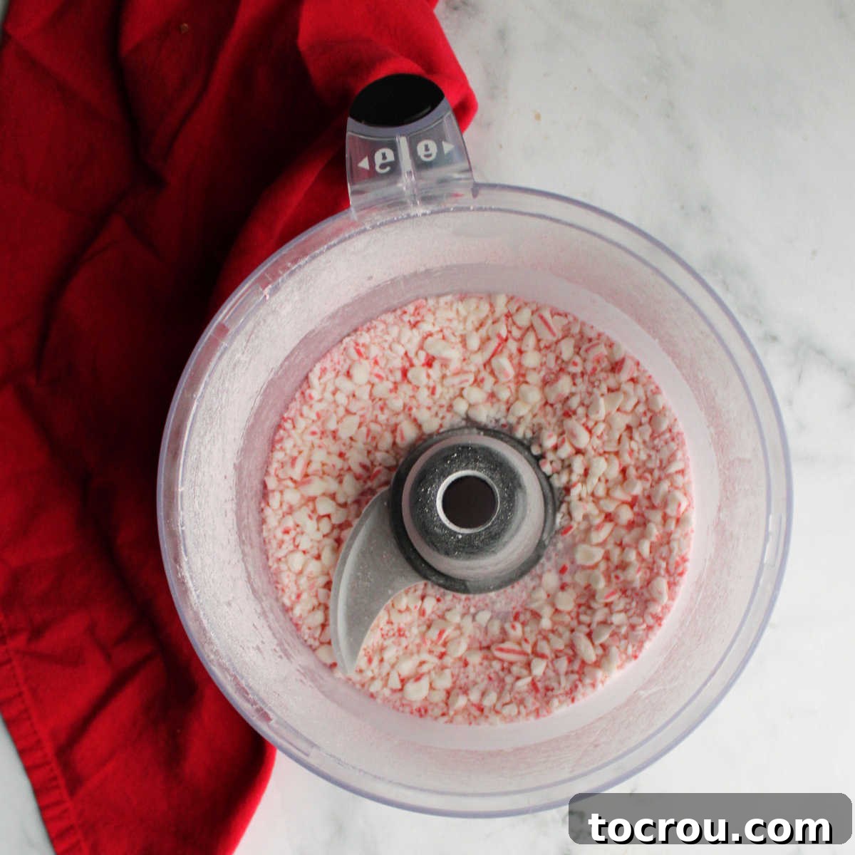 Food processor containing finely crushed candy cane bits, ready to be incorporated into the cheesecake filling.
