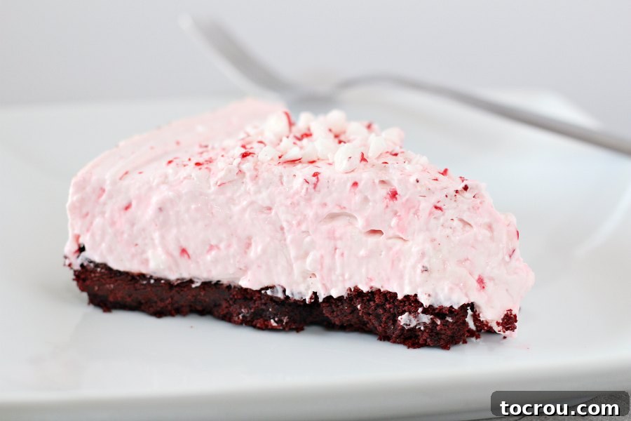 A perfectly sliced piece of no bake candy cane cheesecake, showcasing the rich red velvet Oreo crust and the creamy peppermint filling, ready for serving.
