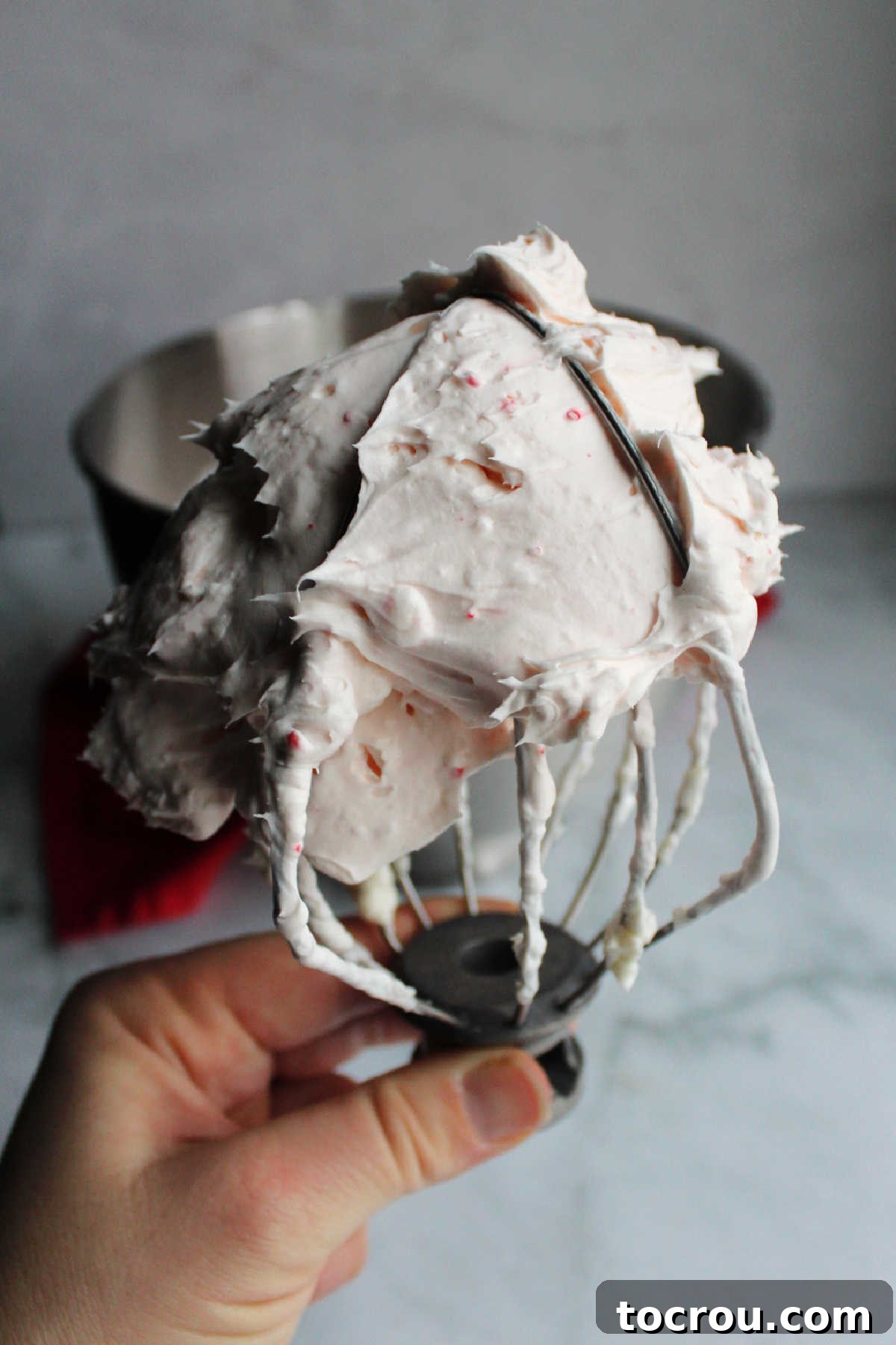 A beater covered in a light and fluffy candy cane cream cheese mixture, showcasing the perfect consistency for the cheesecake filling.
