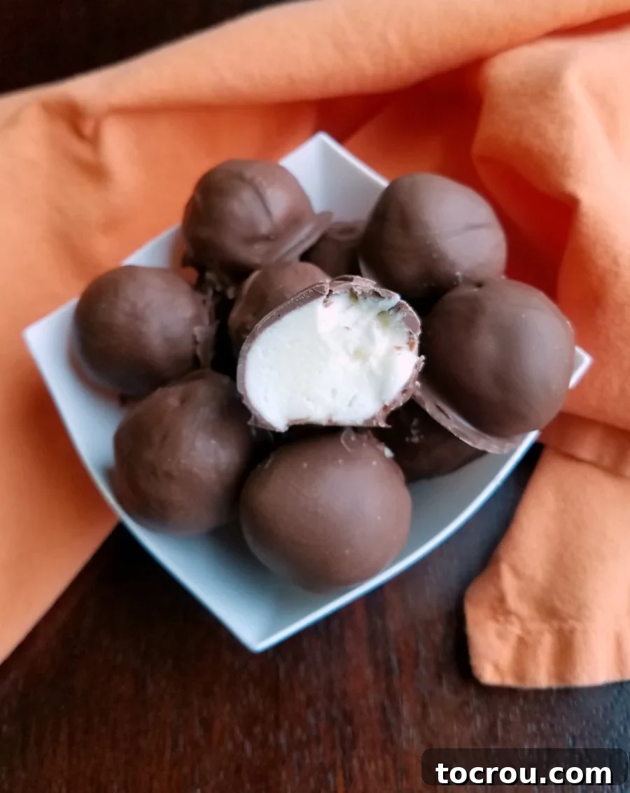 Chocolate Covered Orange Cheesecake Truffles A bowl of glossy chocolate-coated truffles, with one cut in half to reveal its creamy white orange-flavored cream cheese center.