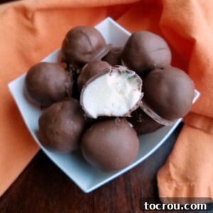 Chocolate Orange Cheesecake Truffles Bowl of chocolate coated truffles with one cut in half on top showing the white orange flavored cream cheese center.