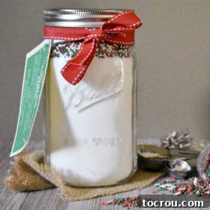 Glass jar filled with sugar cookie mix and sprinkles with gift tag.