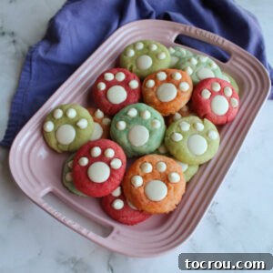 Pink platter filled with colorful orange, pink, blue and green paw print cookies with white chocolate paws on top.