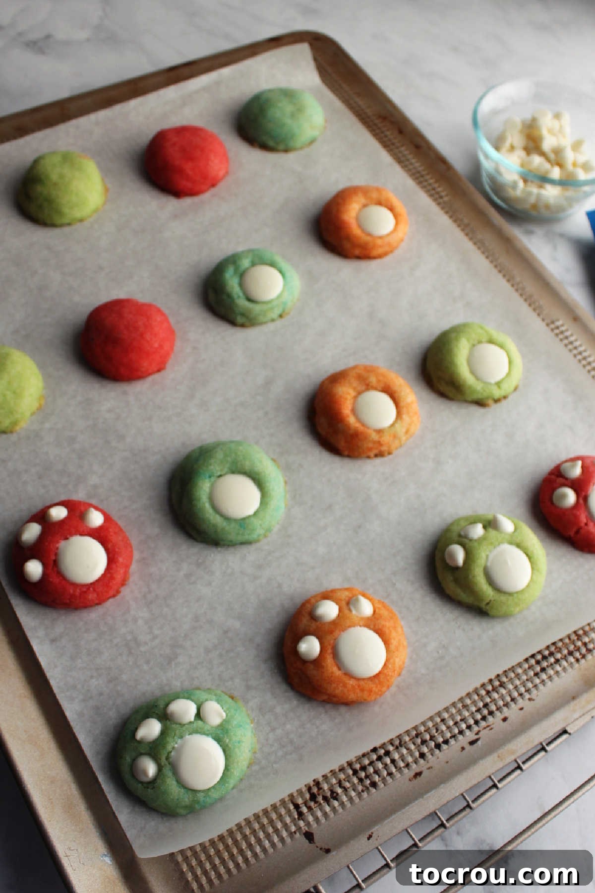 The simple process of decorating freshly baked Jell-O cookies by pressing white melting disks and small baking chips into them to form charming paw print designs.
