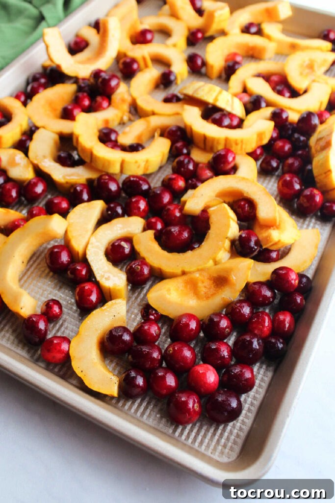 Sliced delicata squash and fresh cranberries on a baking sheet pan, ready for roasting.