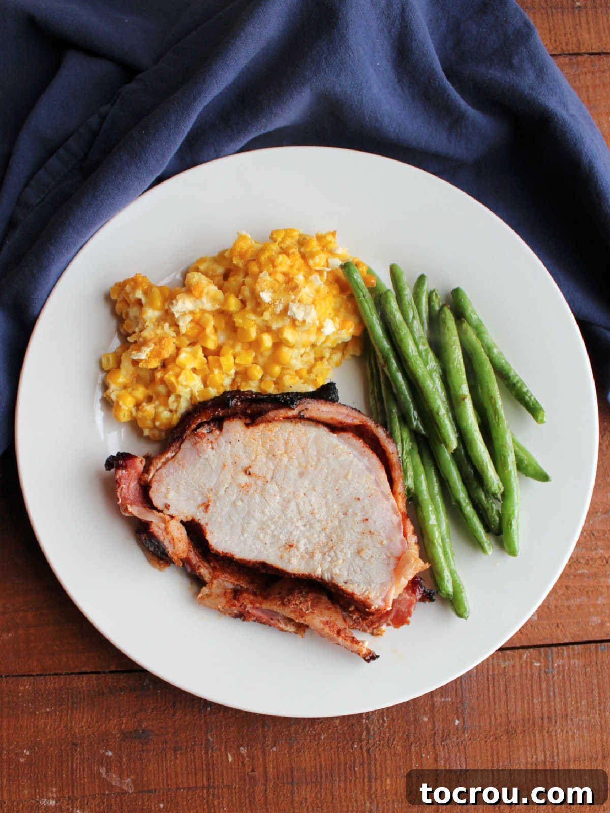Dinner plate with scalloped corn, roasted green beans, and a piece of bacon wrapped pork loin.
