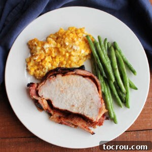 Dinner plate with bacon wrapped smoked pork loin, roasted green beans, and scalloped corn on it, ready to eat.