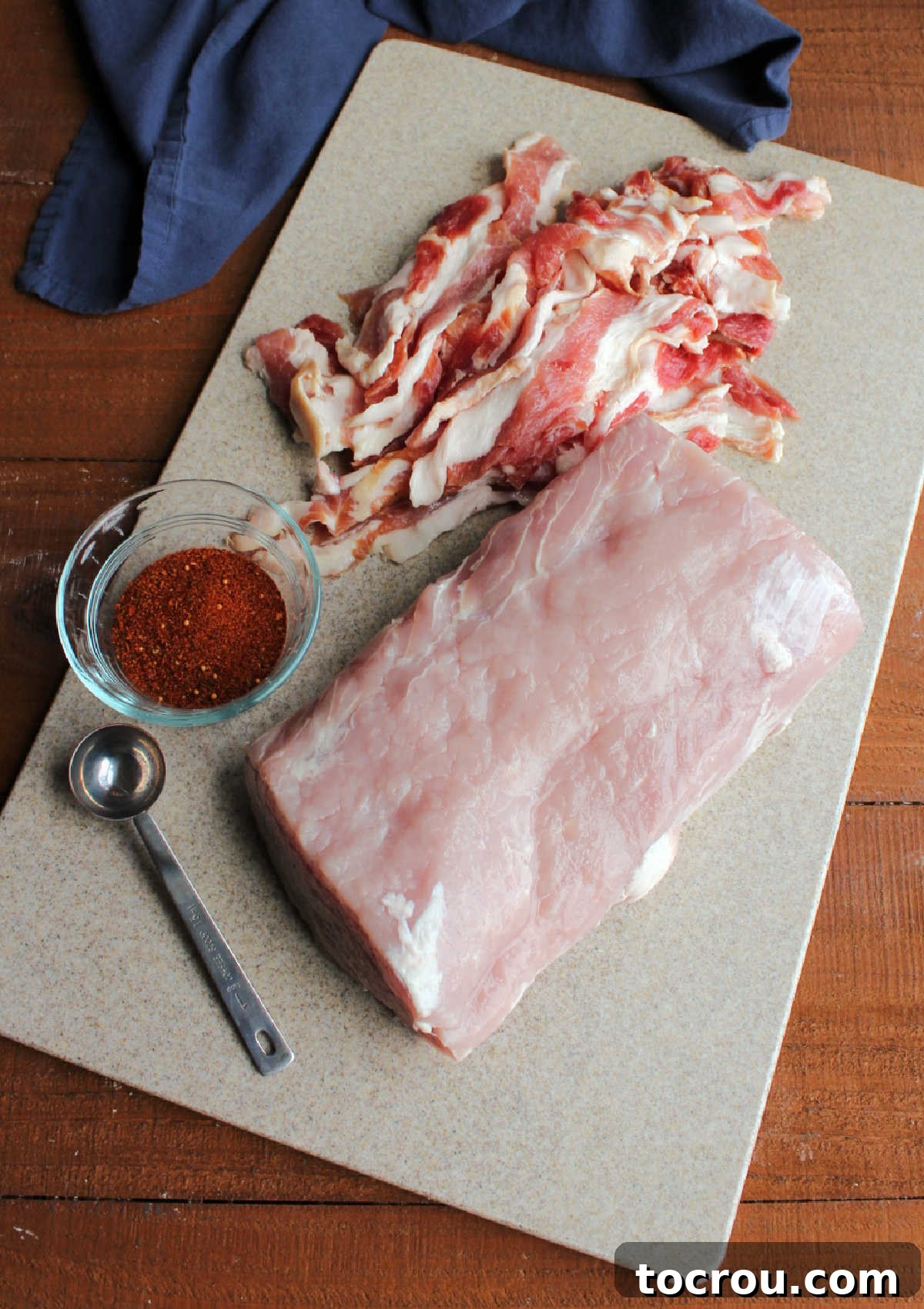 Raw pork loin, bacon, and BBQ rub on a cutting board.
