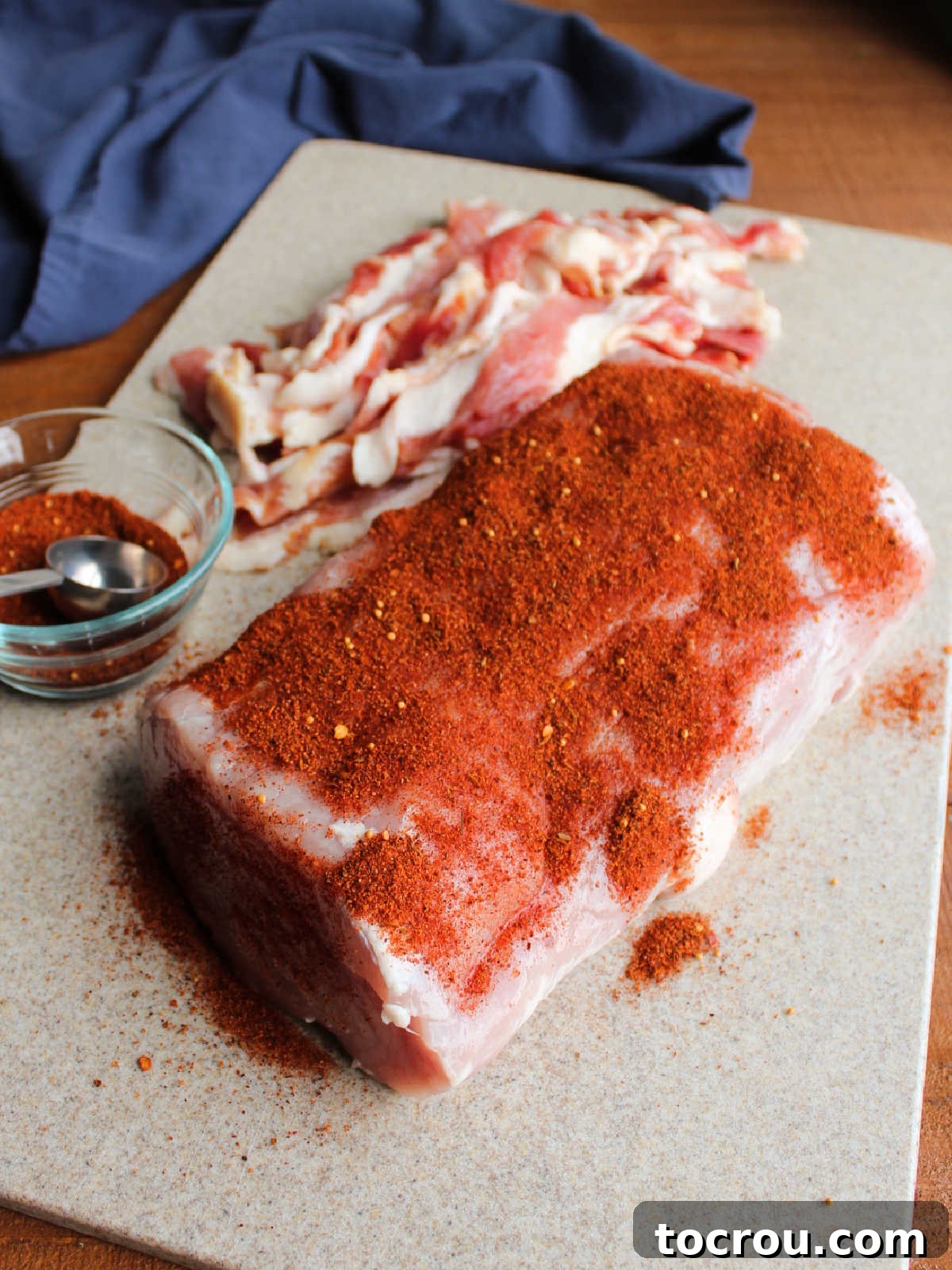 Pork loin coated heavily in BBQ rub, ready to be wrapped in bacon.