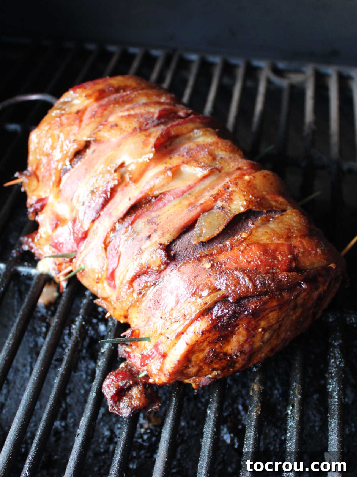 Smoked bacon wrapped pork loin ready to come off the smoker, showing more cooked bacon.