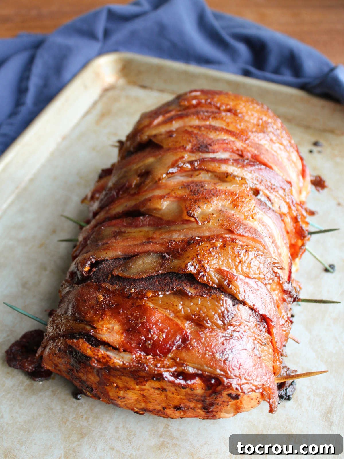 Fully cooked smoked bacon wrapped pork loin on sheet pan, resting before being sliced.