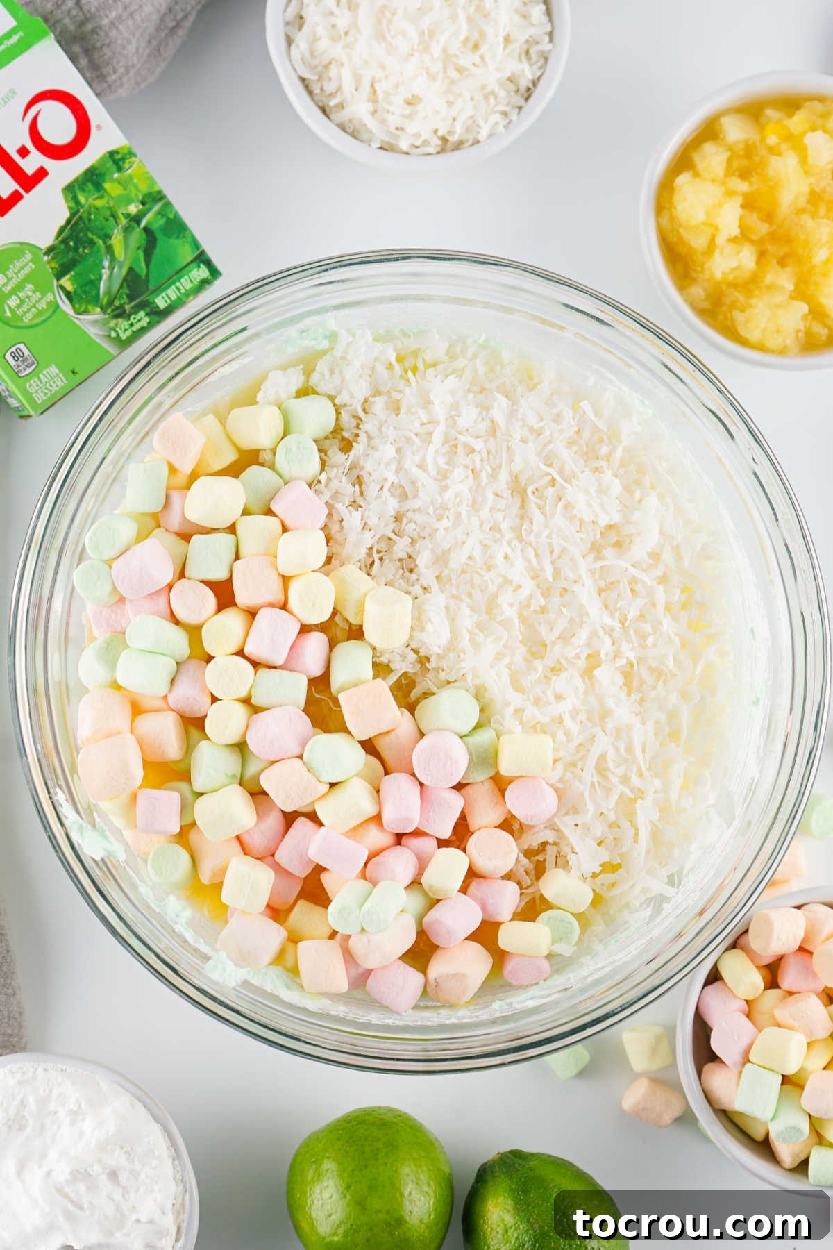 Adding fruity marshmallows and shredded coconut to the seafoam salad mixture.
