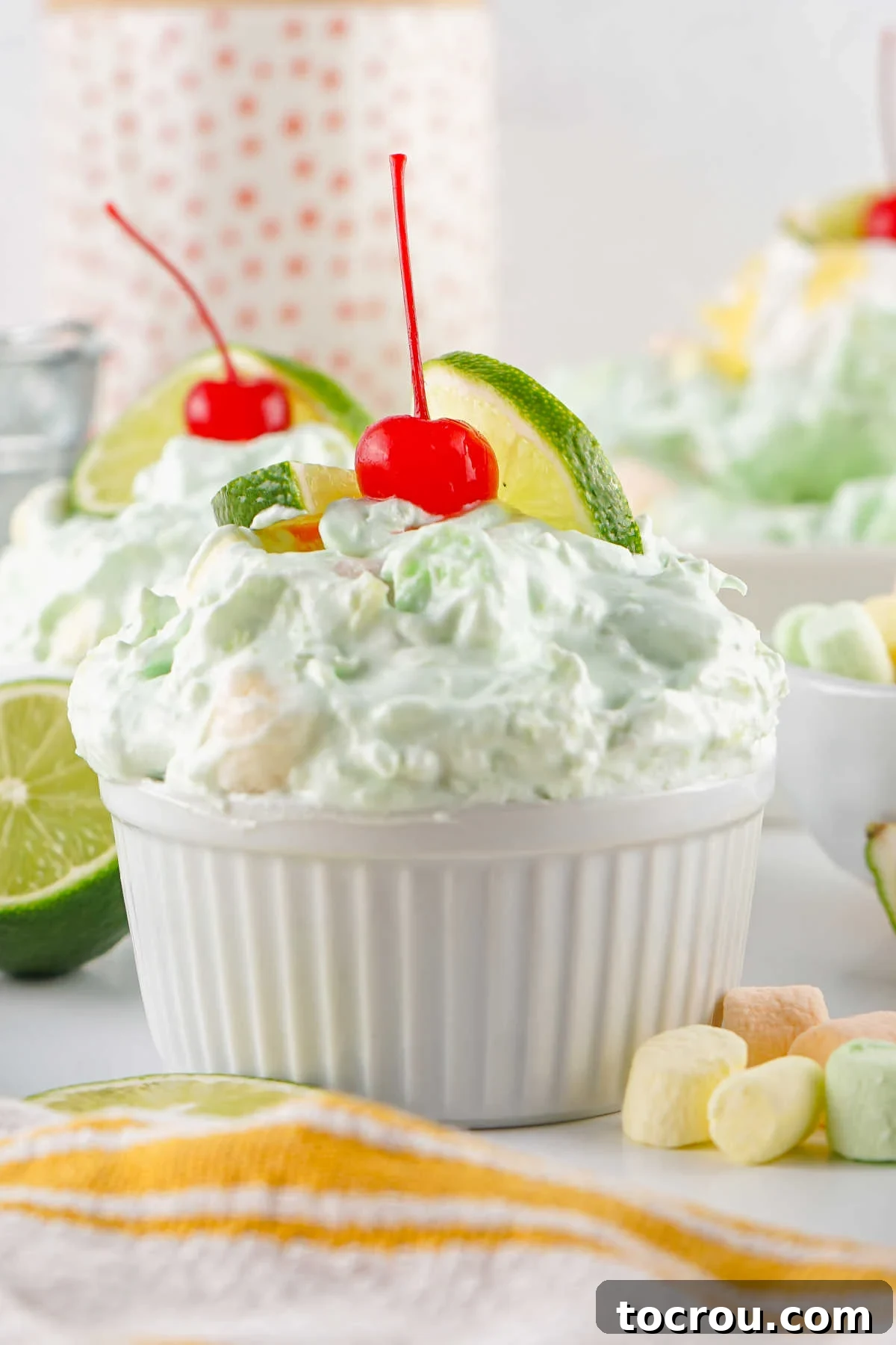 Ramekins fill with lime fluff seafoam salad, topped with a maraschino cherry, ready to eat.