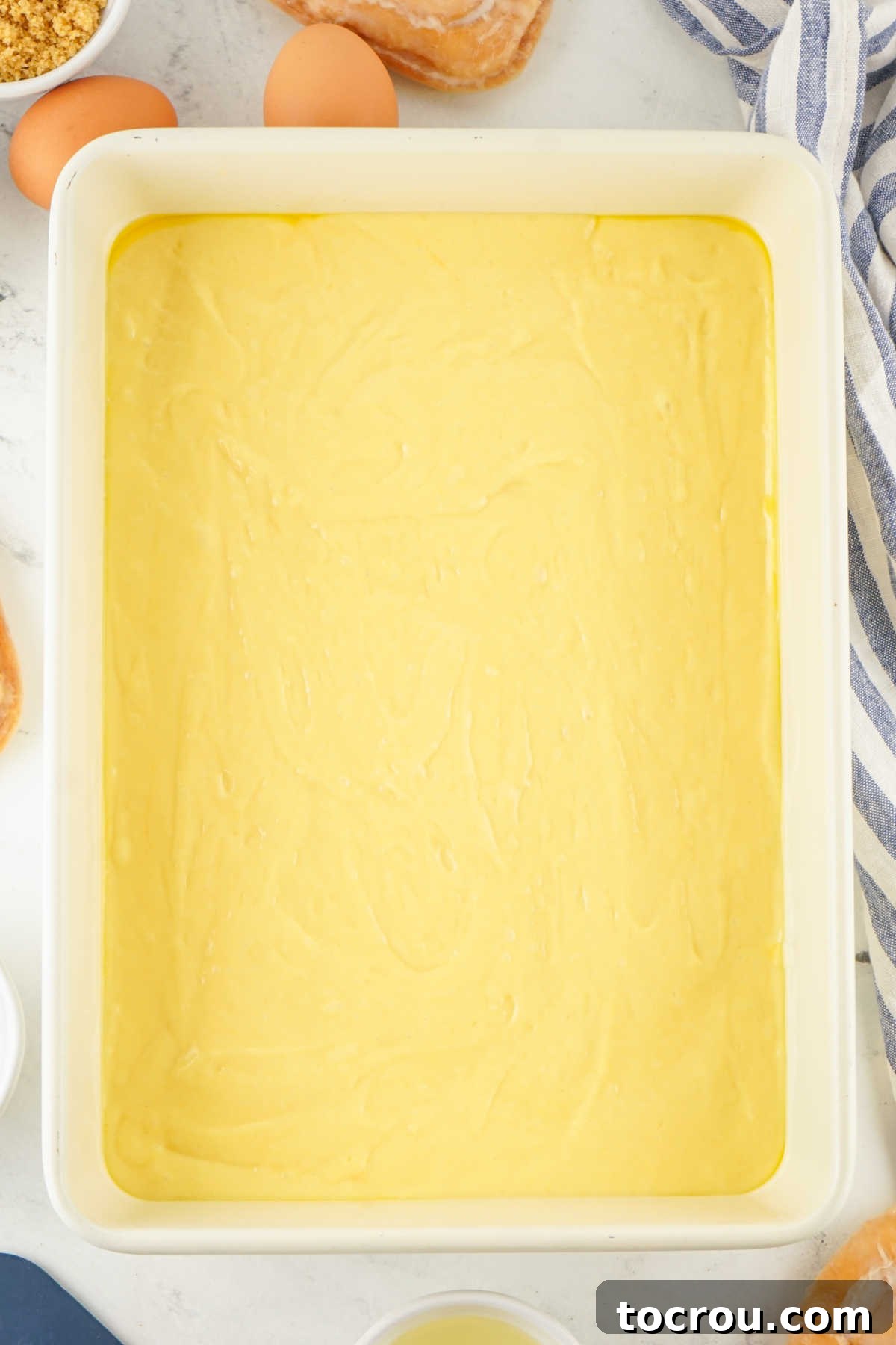 Doctored up vanilla cake mix batter spread smoothly in the bottom of a 9x13 inch baking pan, ready for the cinnamon sugar layer.