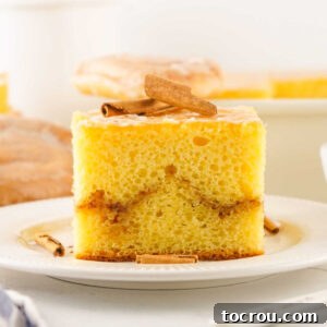 Piece of honey bun cake with cinnamon brown sugar layer in the middle, rich yellow cake, and light glaze on top.