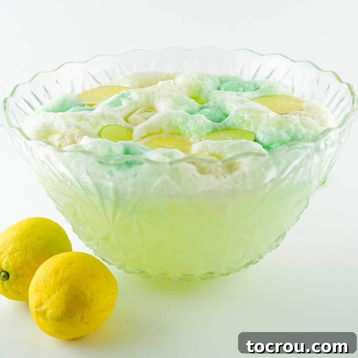 Side view of punch bowl filled with pale green punch topped with scoops of lemon and lime sherbet with a little bit of pastel foam from the sherbet and soda.
