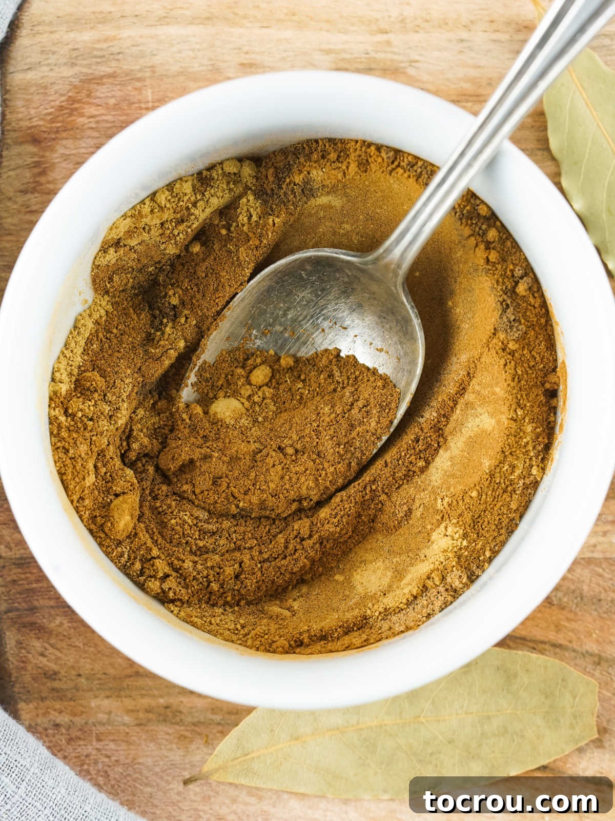 Small bowl filled with the spice powders, getting stirred together with a spoon to create homemade pumpkin pie spice. 