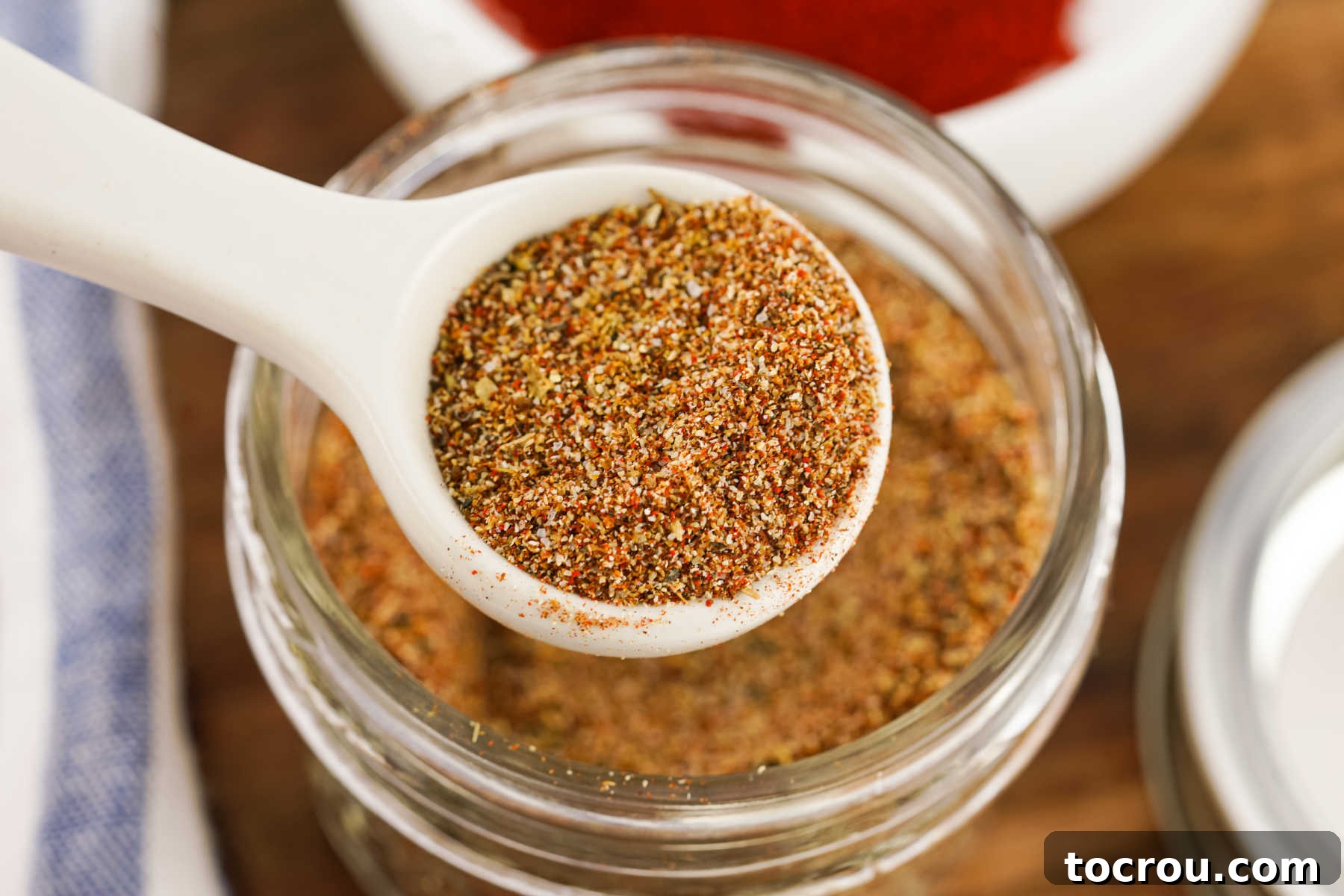 Homemade Taco Seasoning Small spoon with a scoop of homemade taco seasoning over the jar with the remaining seasoning mix inside.