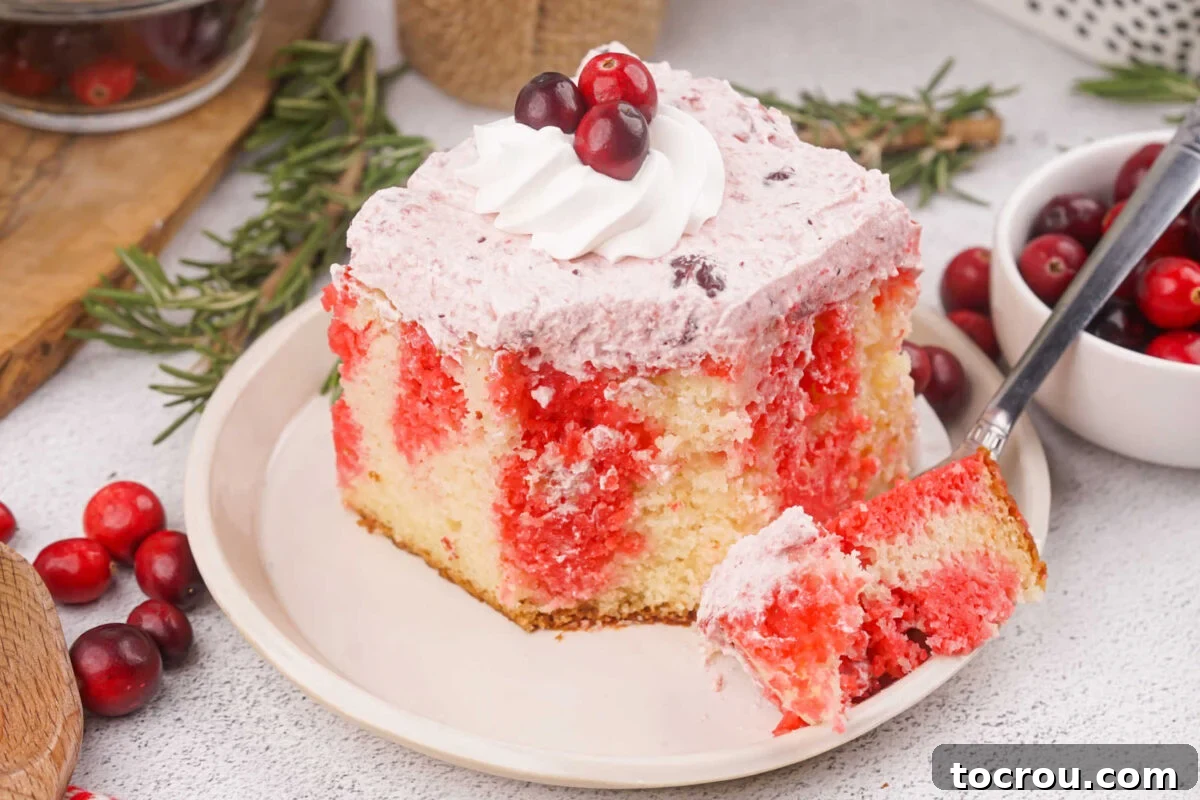 Ruby Cranberry Infusion Cake 2 Dessert plate with square piece of cranberry poke cake with red jello stripes in white cake topped with creamy cranberry frosting, bite on fork ready to eat.