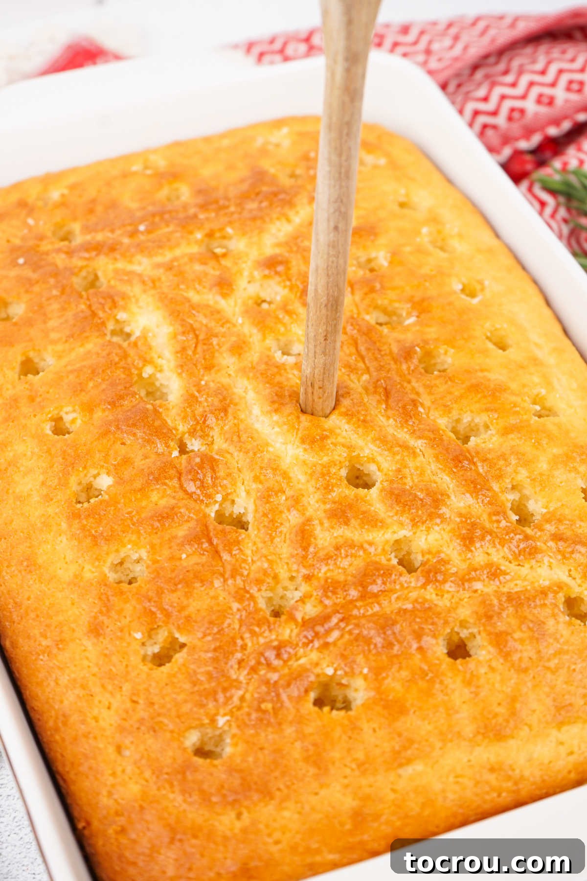 Ruby Cranberry Infusion Cake 4 Using the handle of a wooden spoon to poke holes into baked vanilla cake.