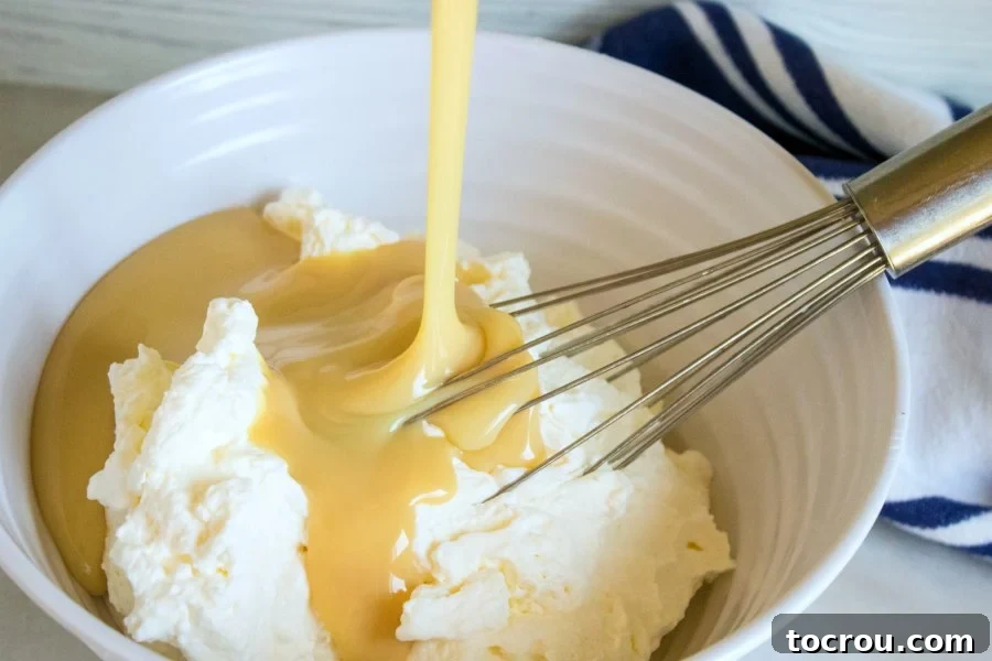 Patriotic Swirl No-Churn Delight 3 Sweetened condensed milk being poured into a bowl of fluffy whipped cream, the essential base for no-churn ice cream.