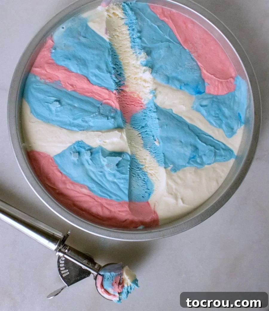 Patriotic Swirl No-Churn Delight 5 An ice cream scoop digging into a pan of red, white, and blue no-churn ice cream, showing its creamy texture.
