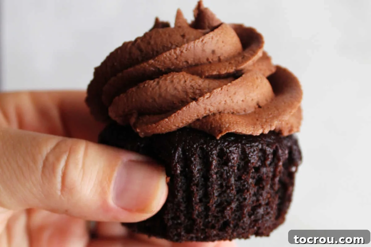 Crazy Delicious Chocolate Cupcakes 2 Hand holding a chocolate crazy cake cupcake without the wrapper showing deep brown chocolate color and moist cake crumb.
