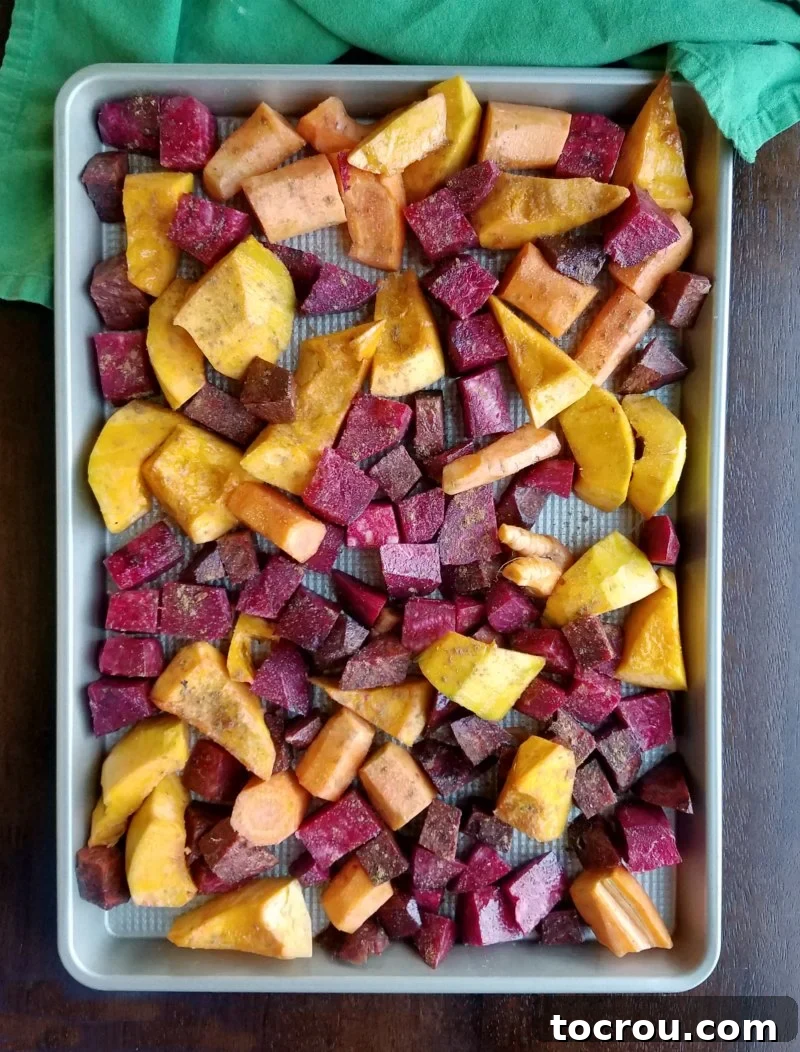 Baking sheet of squash and root veggies tossed in Chinese five spice, ready to enter the oven for roasting.