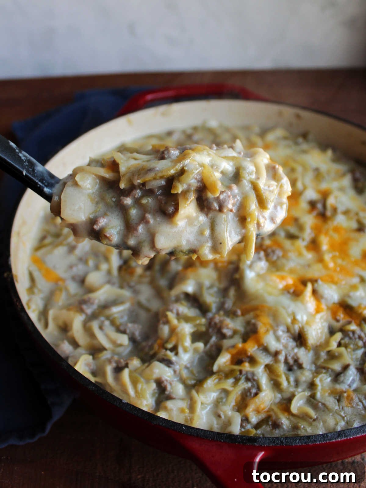 Serving spoon scooping out a helping of creamy one pot pasta with ground beef and green beans.