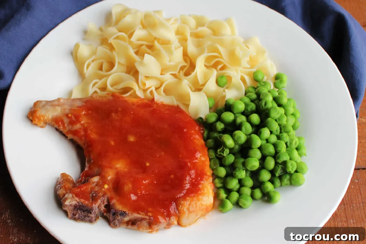 Close up of a sweet and sour pork chop served with peas and noodles. 